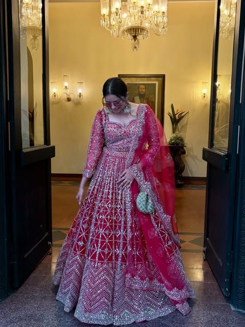 A bride in a rani pink sequin lehenga at a palace doorway